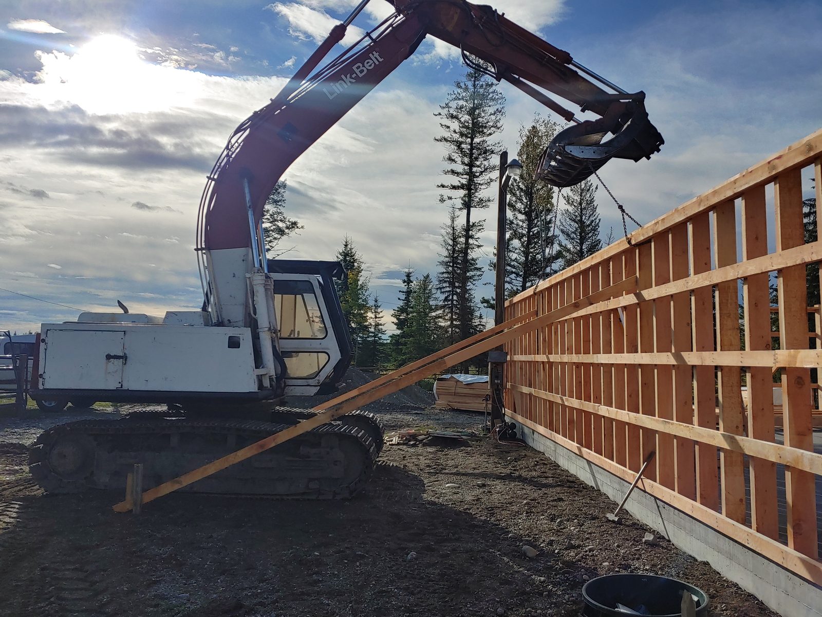 An excavator holding a framed barn wall while it's braced