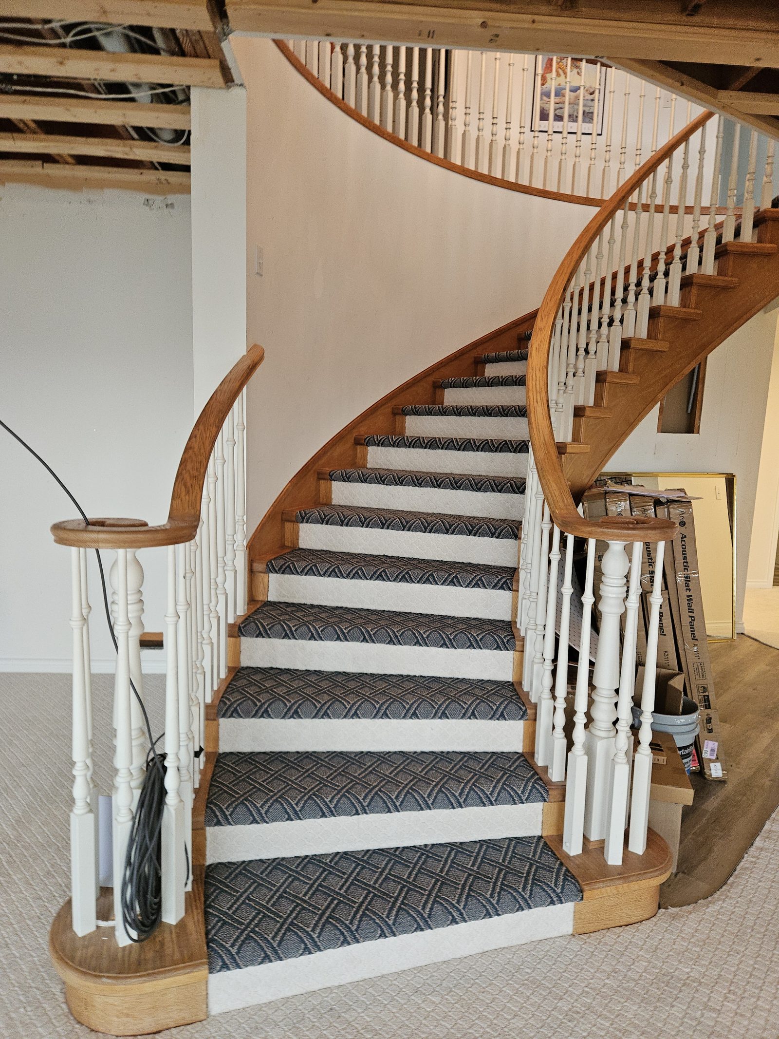A curved staircase with new flooring and repainted spindles during an insurance rebuild