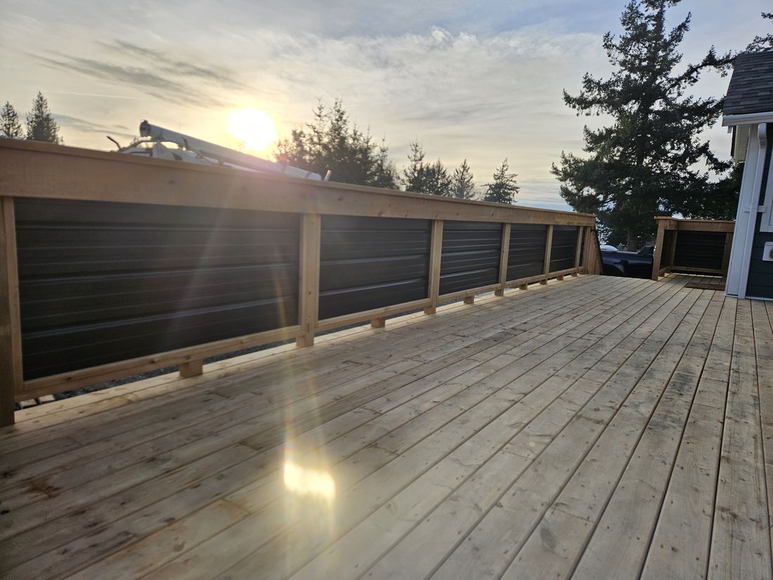 A deck railing with black corrugated metal panel infill at sunset