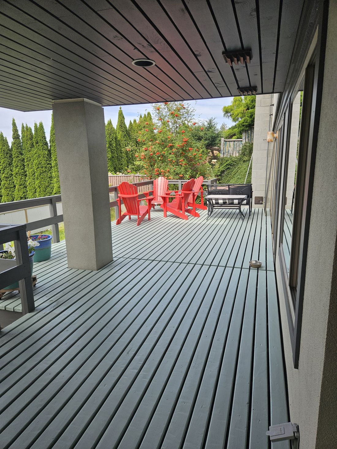 A covered deck stained in seafoam with red chairs