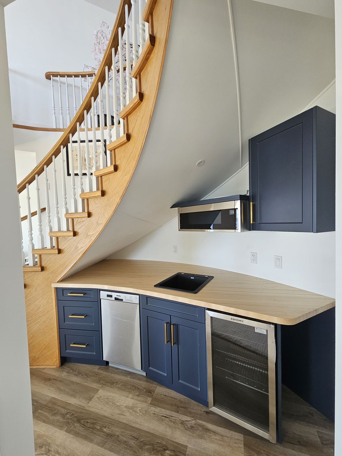 A kitchenette built into the space beneath a curved staircase
