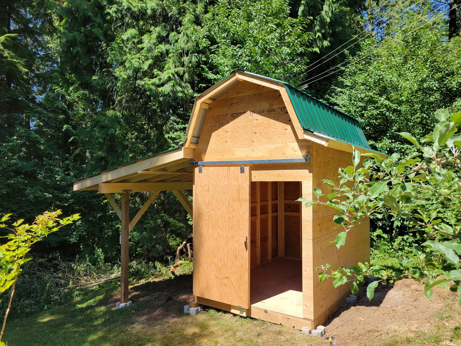 A gambrel-roofed garden shed with a green metal roof and an open lean-to