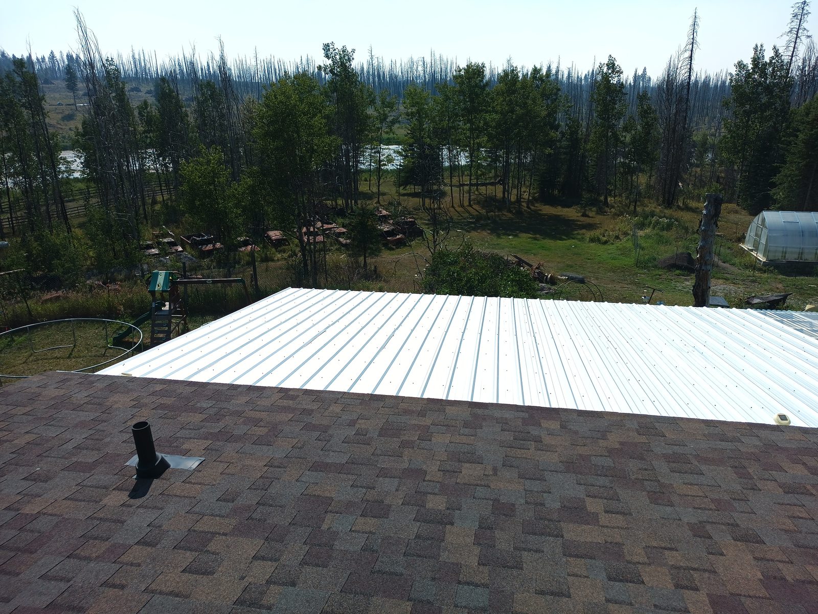 A large Galvalume deck cover built over an existing deck, with wildfire-damaged forest behind